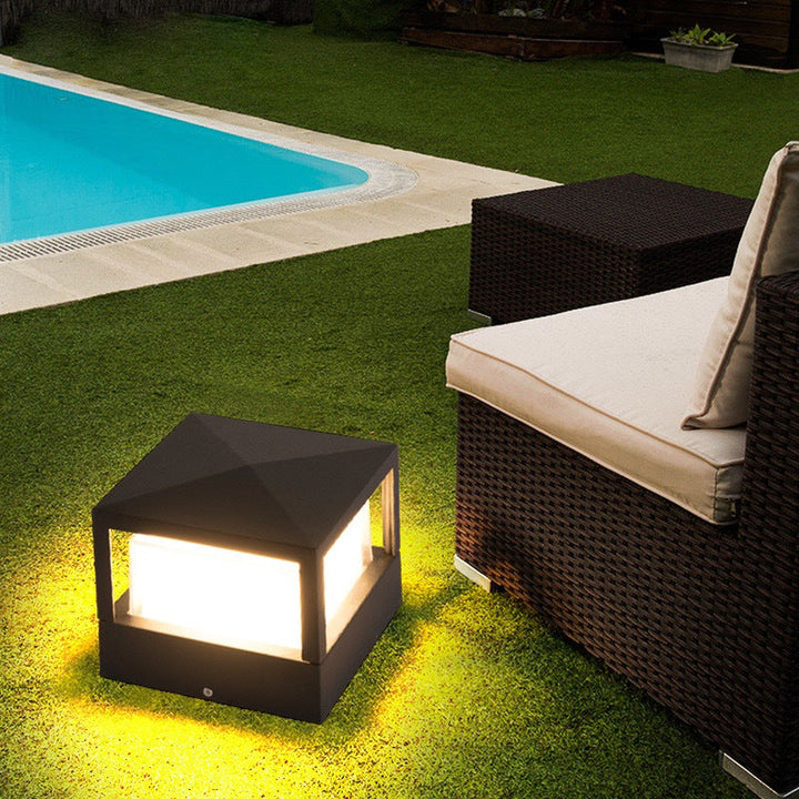Quadratische Leuchte mit Pyramidendach auf einem Rasen neben Pool und Rattan-Sitzmöbel, die das Gras warm beleuchtet. 4