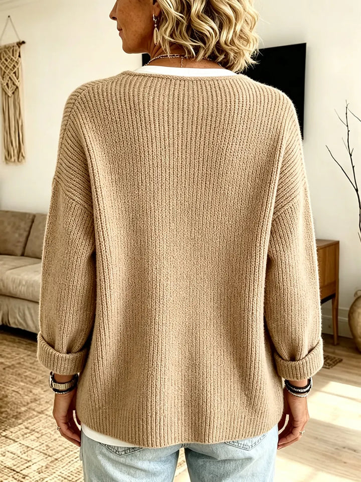 Rückansicht der beigen Strickjacke mit Rippstruktur, umgeschlagenen Ärmelbündchen und lockerem Schnitt, getragen von einer 2