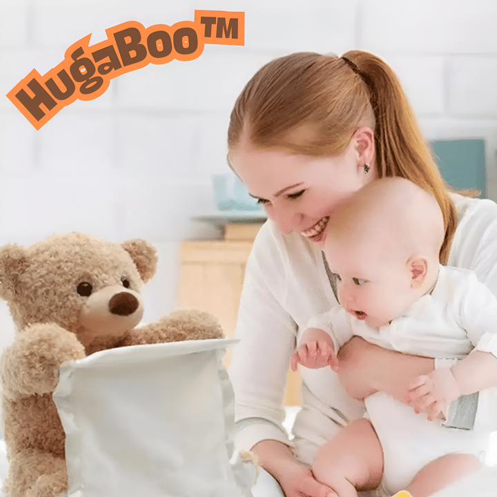 Lächelnde Frau hält ein Baby im Arm und beide schauen auf den hellbraunen Plüschbären, der ein cremefarbenes Tuch hält. 1