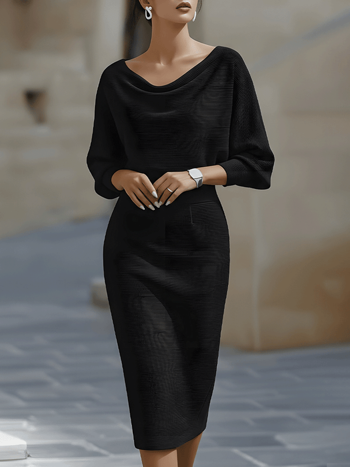 Frontansicht: Model in schwarzem, fein gerippt gestricktem Midikleid mit Wasserfallausschnitt, weiten Fledermausärmeln und enger Taille, im Freien. 1