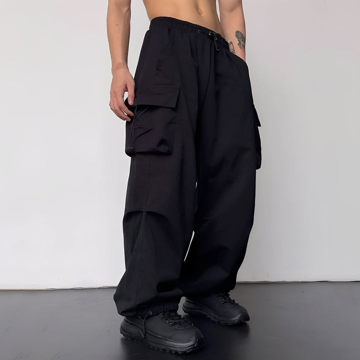 Weite Cargohose in Schwarz, am Model mit schwarzen Sneakern, große Seitentaschen und Kordelzug am Bund 3