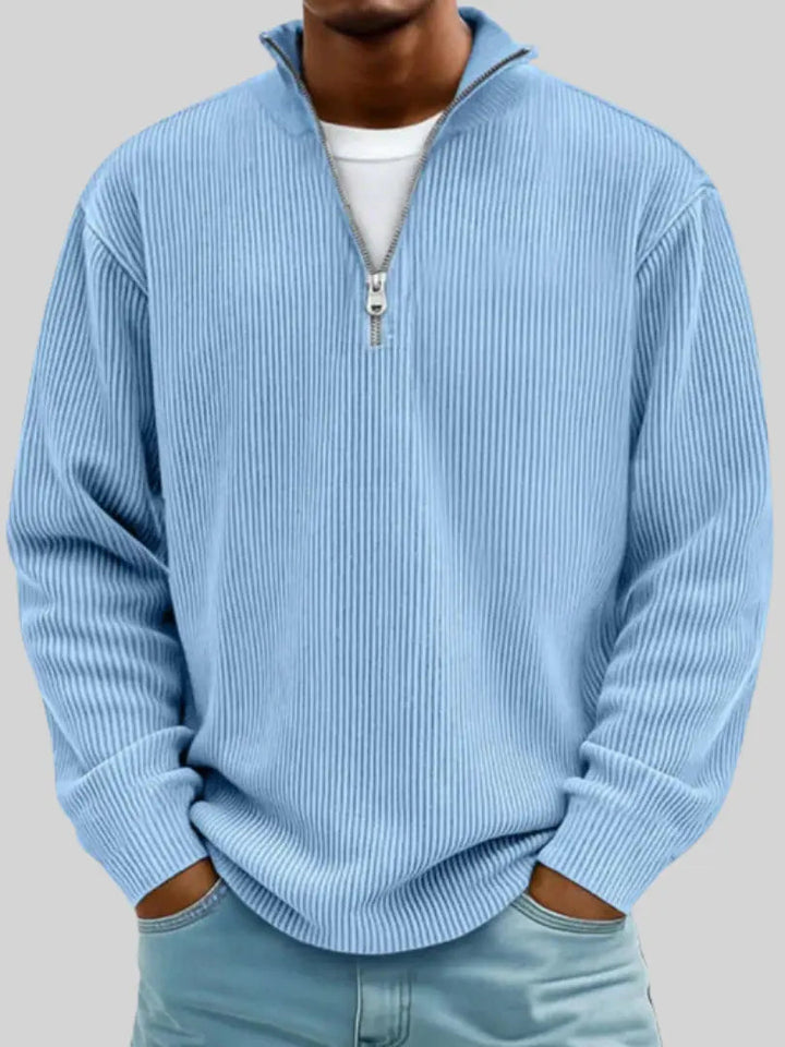 Mann trägt den gerippten Pullover in Hellblau über einem weißen Shirt, Hände in den Hosentaschen, Frontansicht. 1