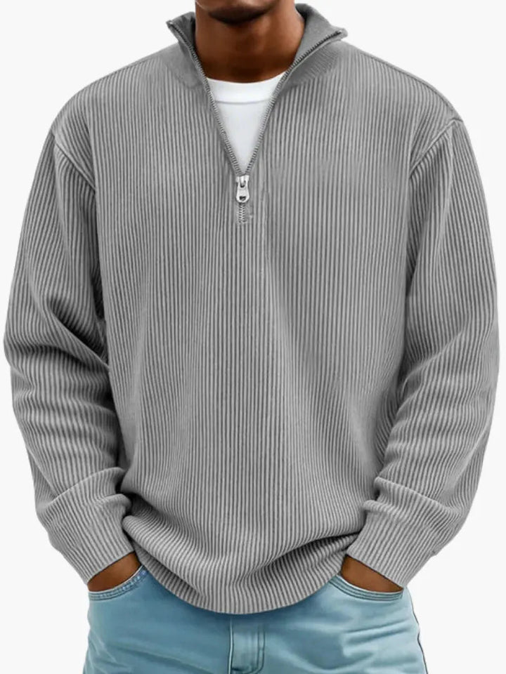 Frontansicht des gerippten Pullovers in Grau mit silbernem Reißverschluss am Stehkragen, getragen über weißem Shirt. 2