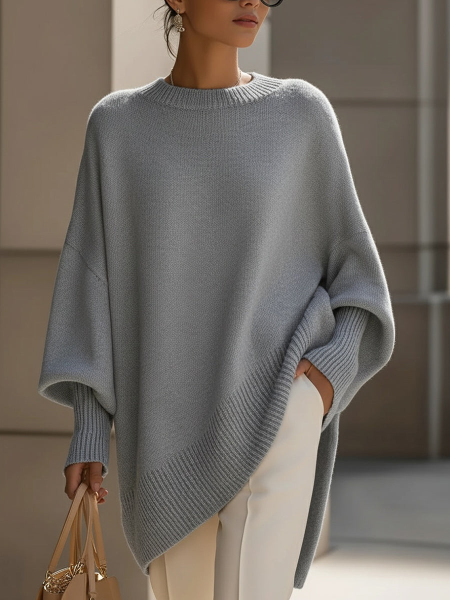 Grauer Strickponcho mit lockerem Schnitt, getragen mit weißer Hose, Hand in der Tasche 10