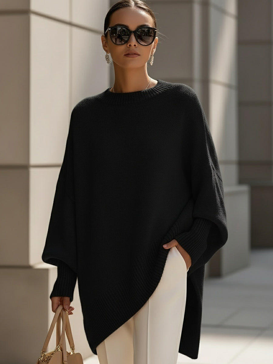 Schwarzer Strickponcho an einer Frau mit Sonnenbrille, weißer Hose und beiger Handtasche vor Steinwand 7