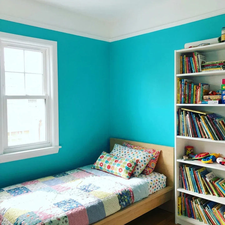 Kinderzimmer mit türkis gestrichenen Wänden, weißen Fensterrahmen, Bett mit Patchworkdecke und einem gefüllten Bücherregal 9