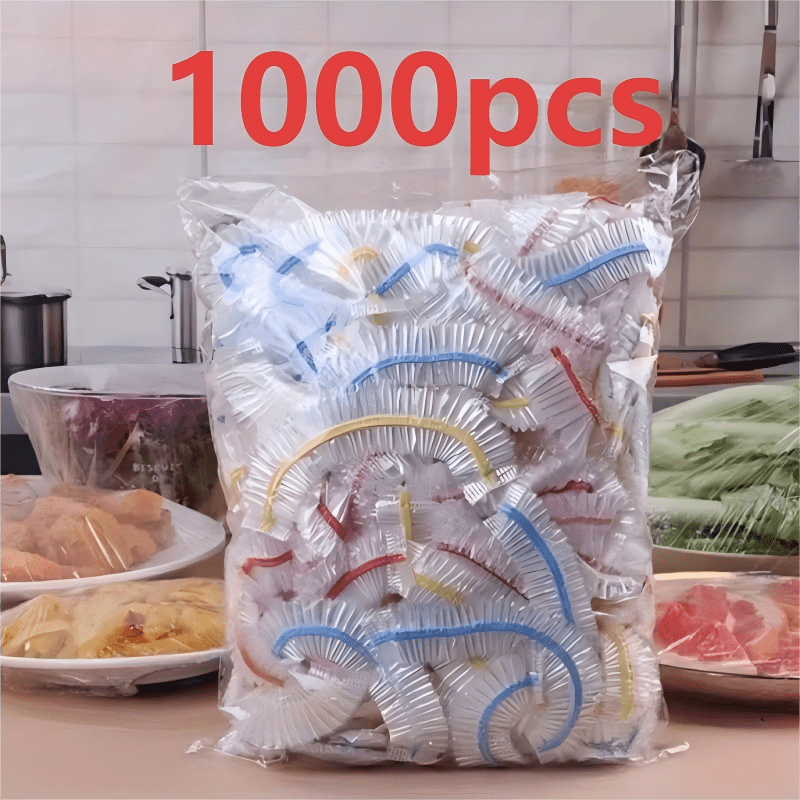 Beutel mit farbig gesäumten Abdeckungen auf einer Küchenarbeitsplatte, dahinter abgedeckte Schalen mit Salat, Fleisch und Nudeln. 3