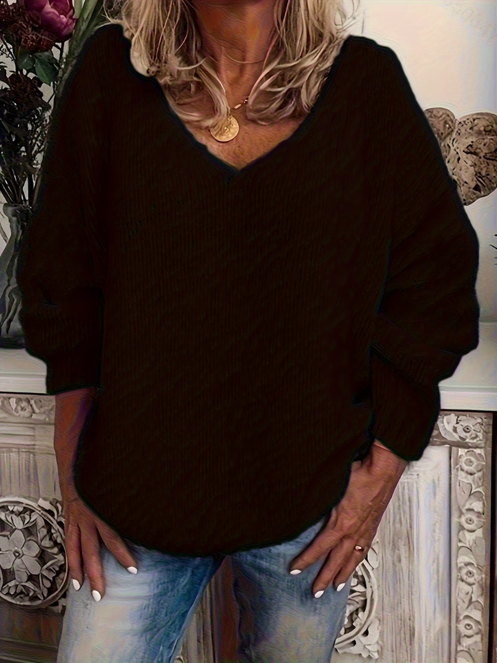 Dunkler, fast schwarzer Strickpullover mit V-Ausschnitt und weiten Ärmeln an einer Frau, die die Hände in die Jeanstaschen steckt. 3