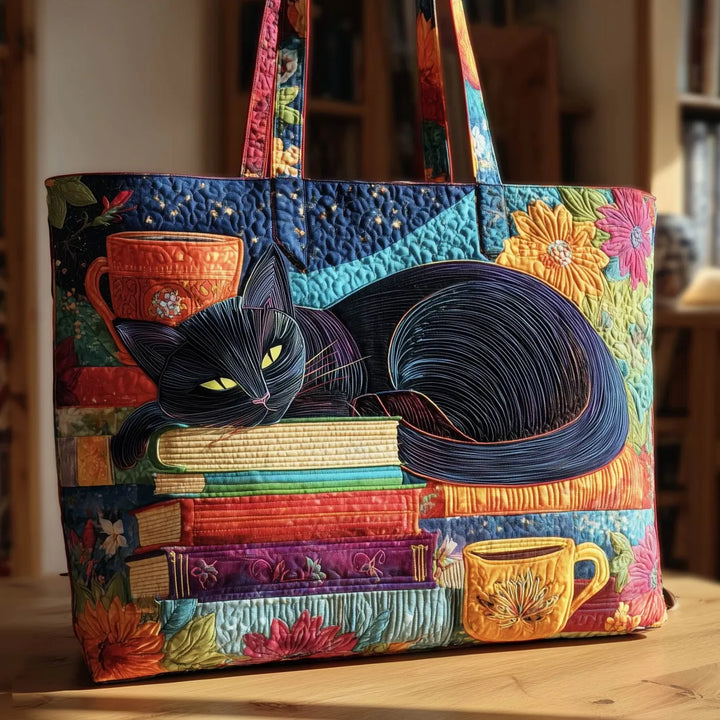 Bunte Steppstofftasche mit schwarzer Katze auf einem Bücherstapel, daneben orange und gelbe Tassen, auf einem Holztisch vor einem Regal. 1