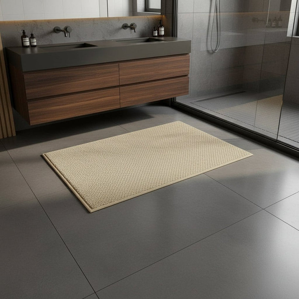 Beige Badematte auf grauem Fliesenboden zwischen Holz-Waschtisch und gläserner Dusche 2