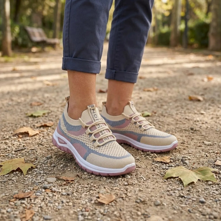 Beige-rosa Sneaker an den Füßen einer Frau im Park, hochgekrempelte blaue Hose, Kiesweg mit Herbstlaub. 29