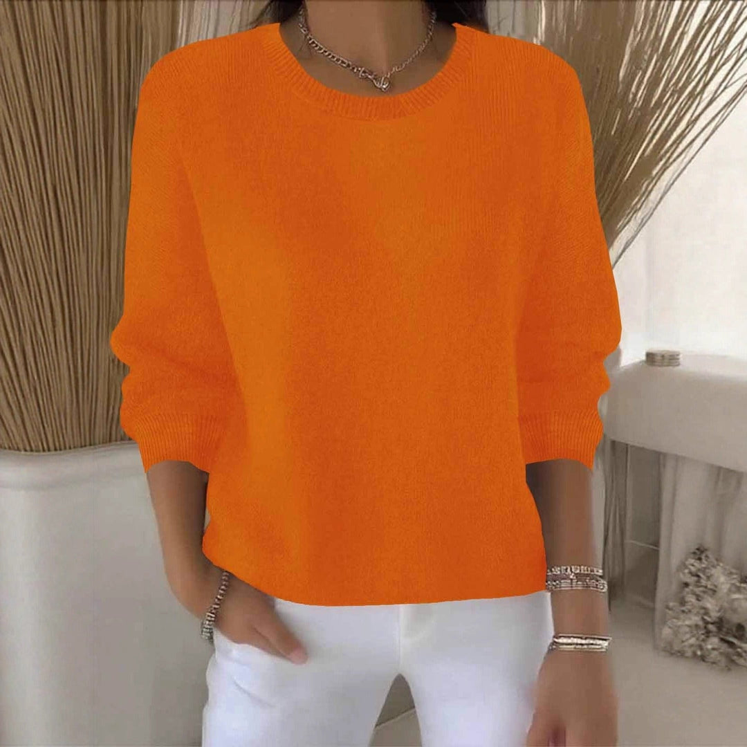 Orangefarbene Variante des Strickpullovers am Model, Frontansicht vor hellem Hintergrund mit Pampasgras 11