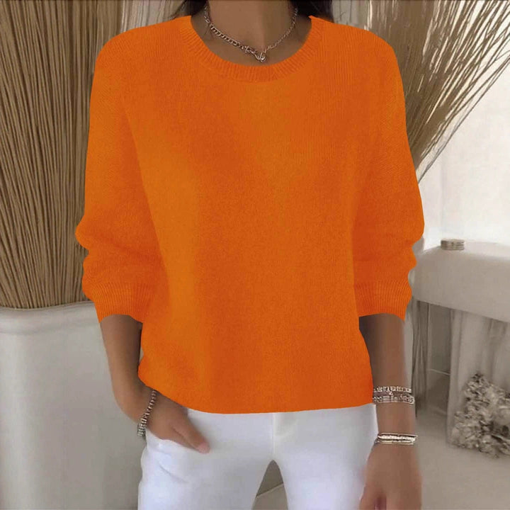 Orangefarbene Variante des Strickpullovers am Model, Frontansicht vor hellem Hintergrund mit Pampasgras 11