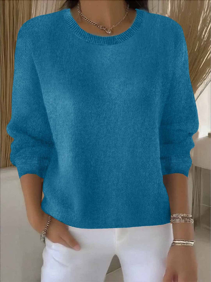 Petrolblaue Variante des Strickpullovers, Frontansicht am Model mit gerippten Ärmelbündchen und weißer Hose 12