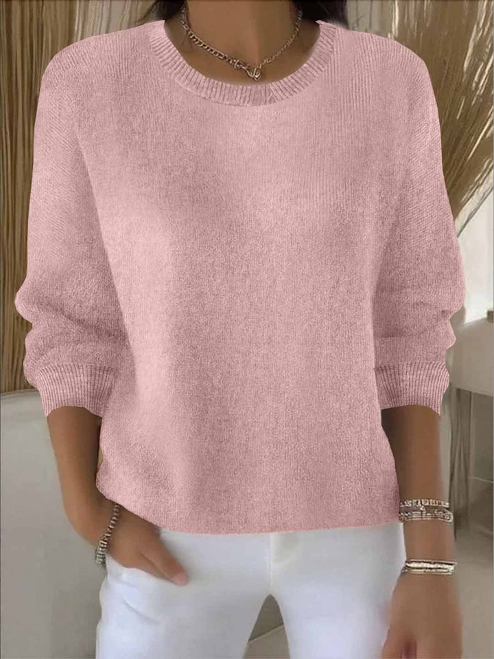 Rosafarbene Variante des Strickpullovers am Model, Rundhalsausschnitt und gerippte Bündchen, kombiniert mit weißer Hose 2