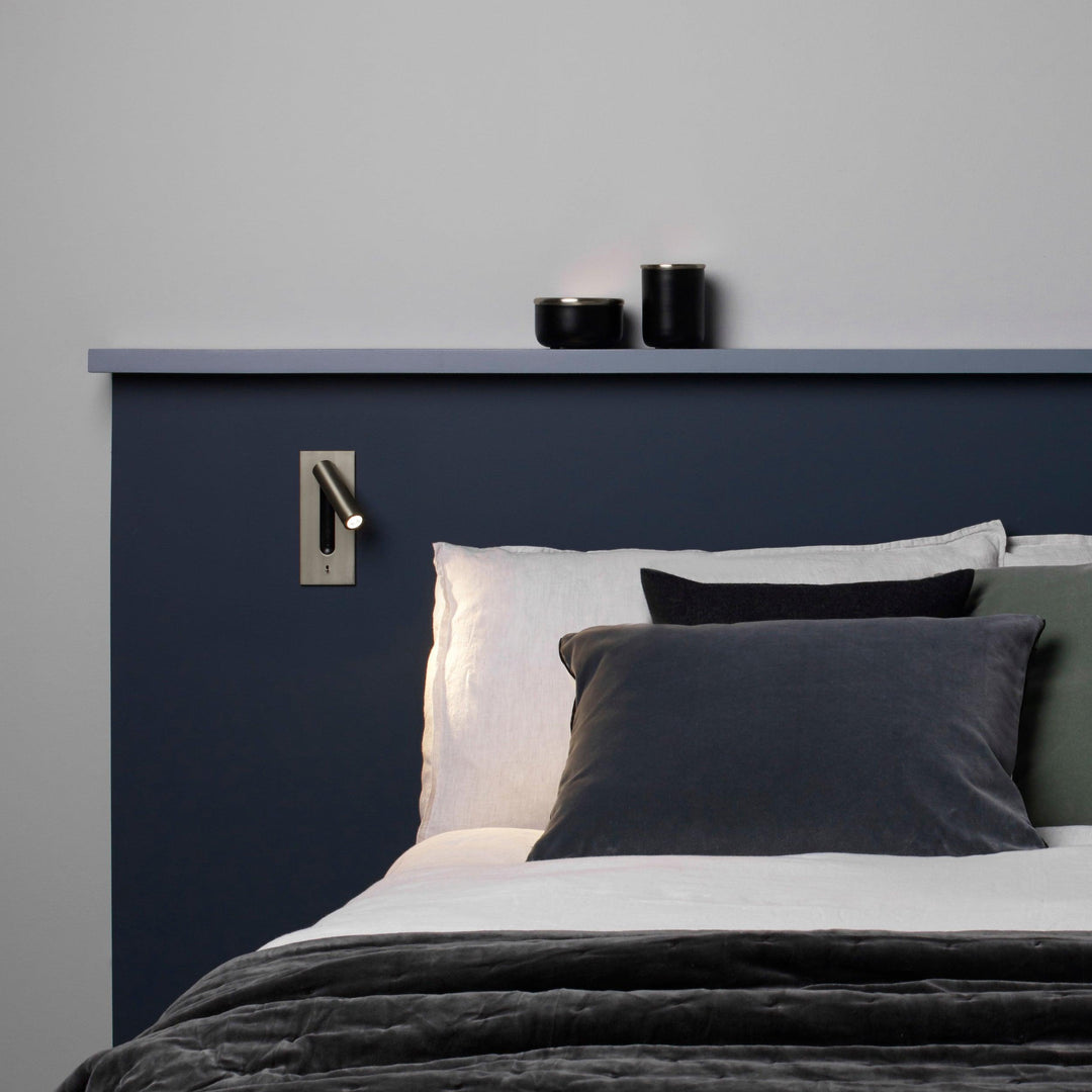 Leuchtende Wandleuchte über dem Kopfteil eines Bettes mit dunkelblauer Wand und grauen Kissen 30