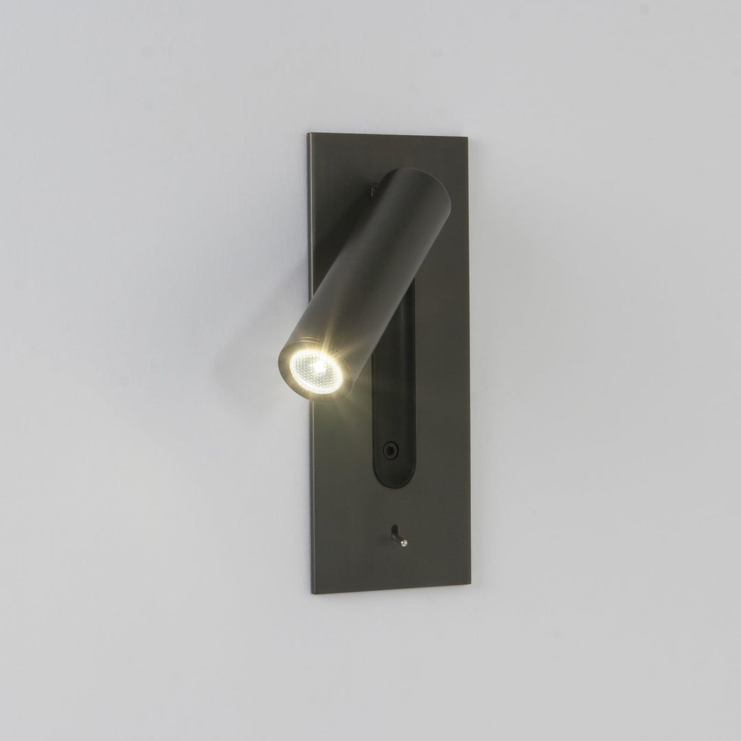 Eingeschaltete Leuchte an heller Wand, Strahler zeigt nach links unten, LED mit Strahlenkranz, dunkle Platte mit 5