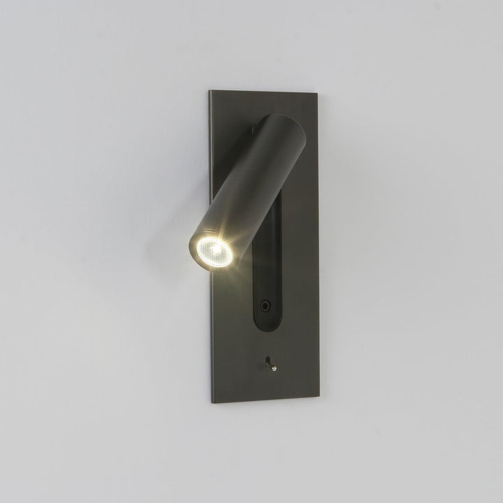 Eingeschaltete Leuchte an heller Wand, Strahler zeigt nach links unten, LED mit Strahlenkranz, dunkle Platte mit 5