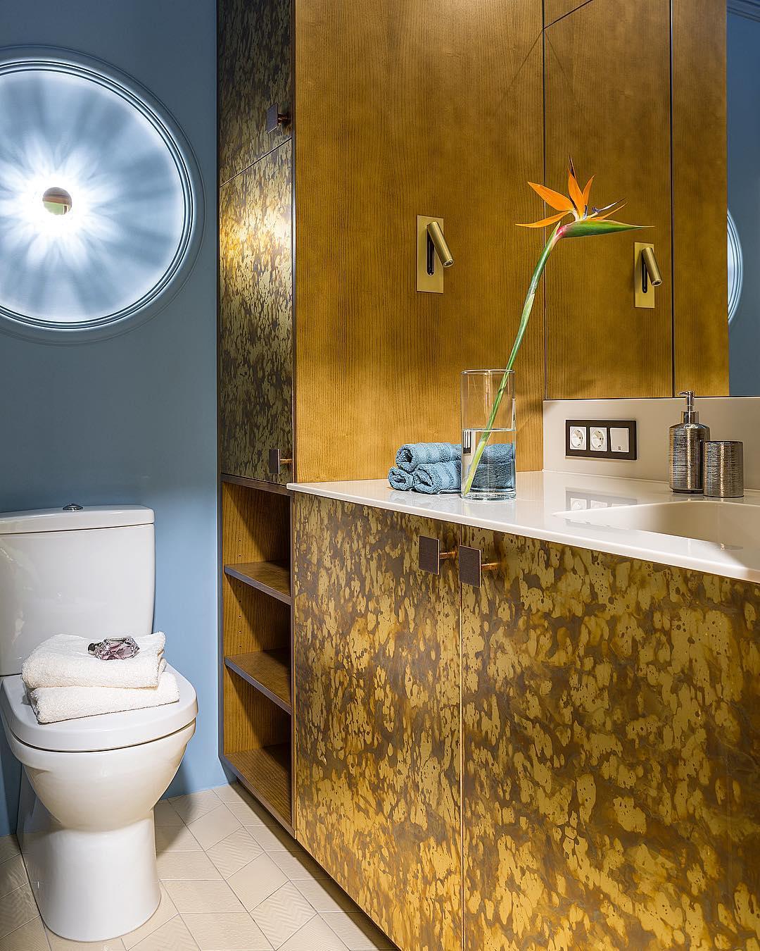 Badezimmer mit goldfarben gemusterten Schrankfronten und Waschtisch, zwei goldfarbene Wandleuchten neben dem Spiegel, Blume 10