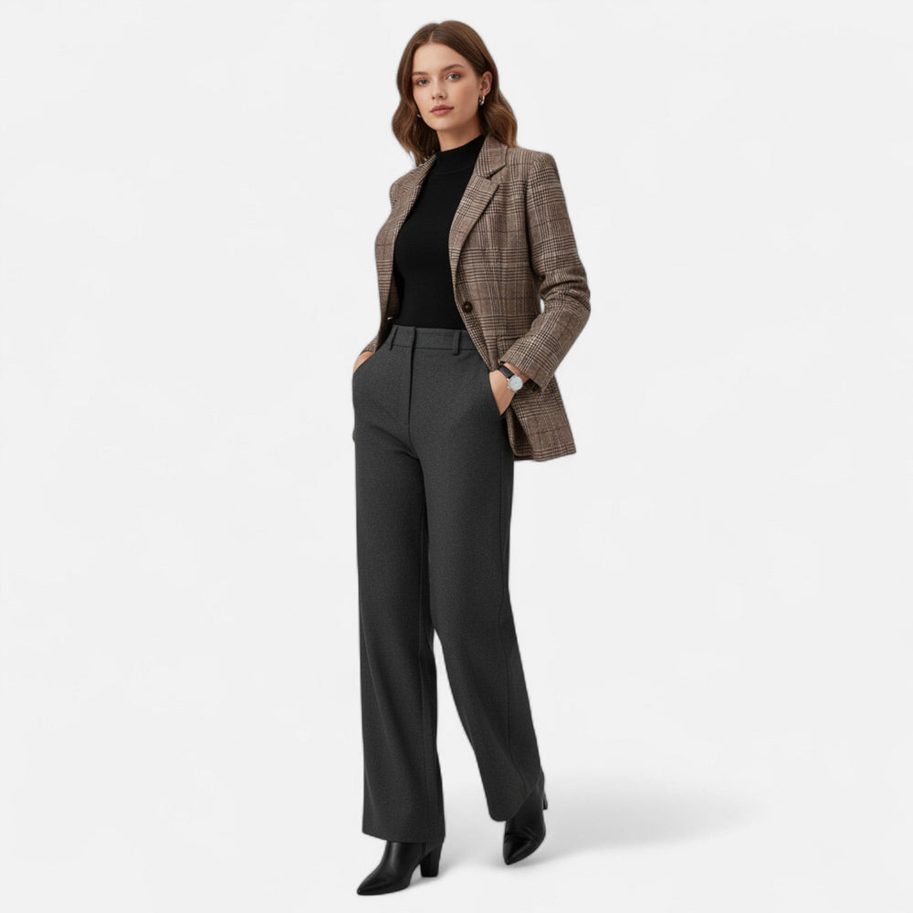 Model in ganzer Figur trägt den karierten Blazer offen zu schwarzem Oberteil, grauer Stoffhose und schwarzen Stiefeletten, Hände in den Taschen. 2
