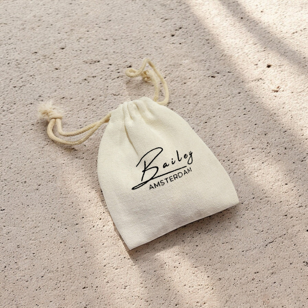 Cremefarbener Stoffbeutel mit Kordelzug als Schmuckverpackung auf sandfarbenem Untergrund mit Schattenspiel 5