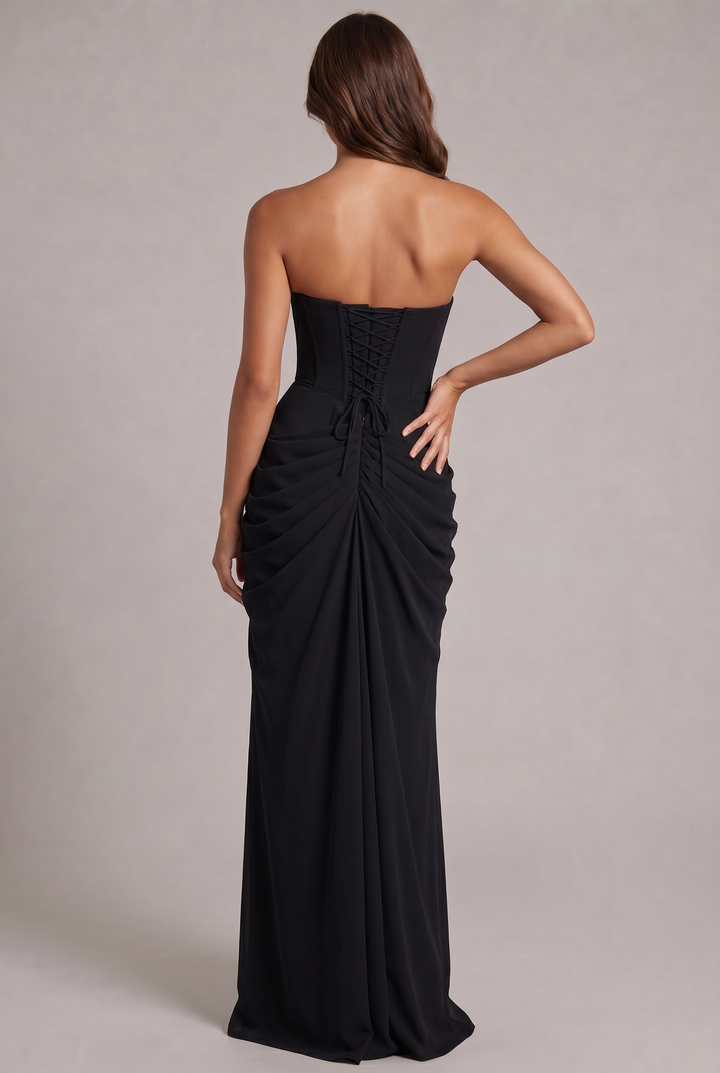 Schwarzes Kleid von hinten: Model mit geschnürtem Corsagenrücken und stark gerafftem, bodenlangem Rock, eine Hand an der 28