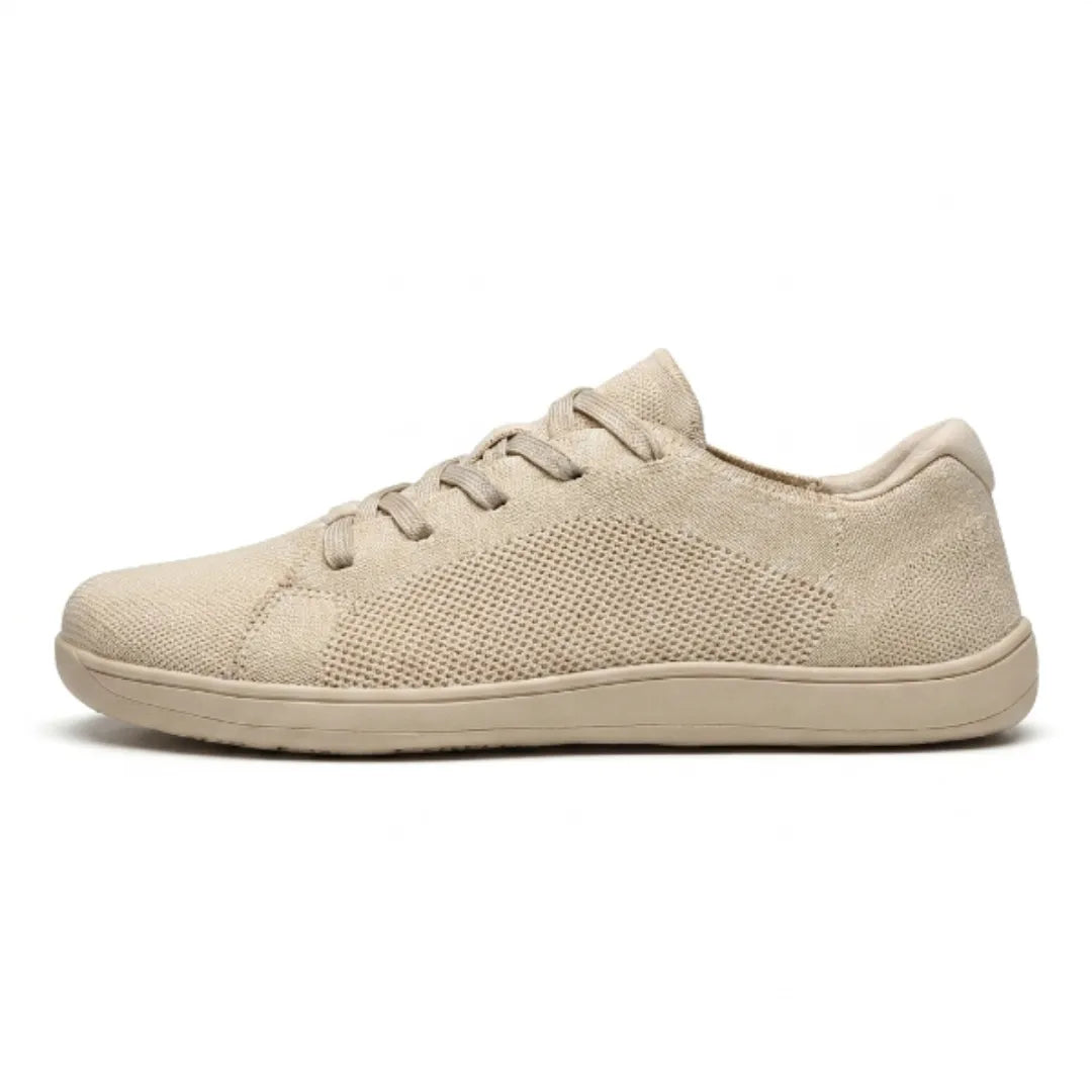 Beiger Mesh-Sneaker in Seitenansicht vor weißem Hintergrund, mit Schnürung, flacher heller Sohle und gelochtem Strickmaterial. 1