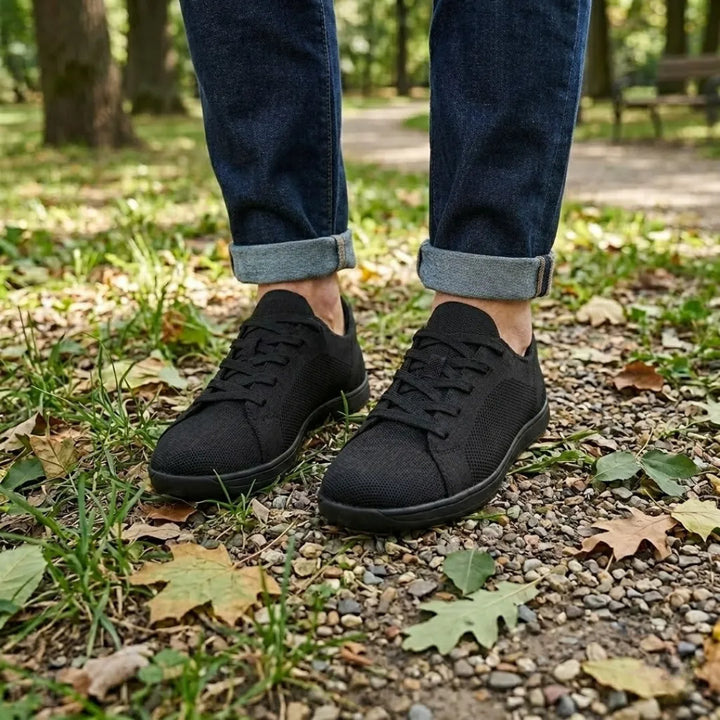 Schwarze Sneaker getragen auf Kiesweg mit Laub und Gras, dazu Jeans mit umgeschlagenem Saum. 11