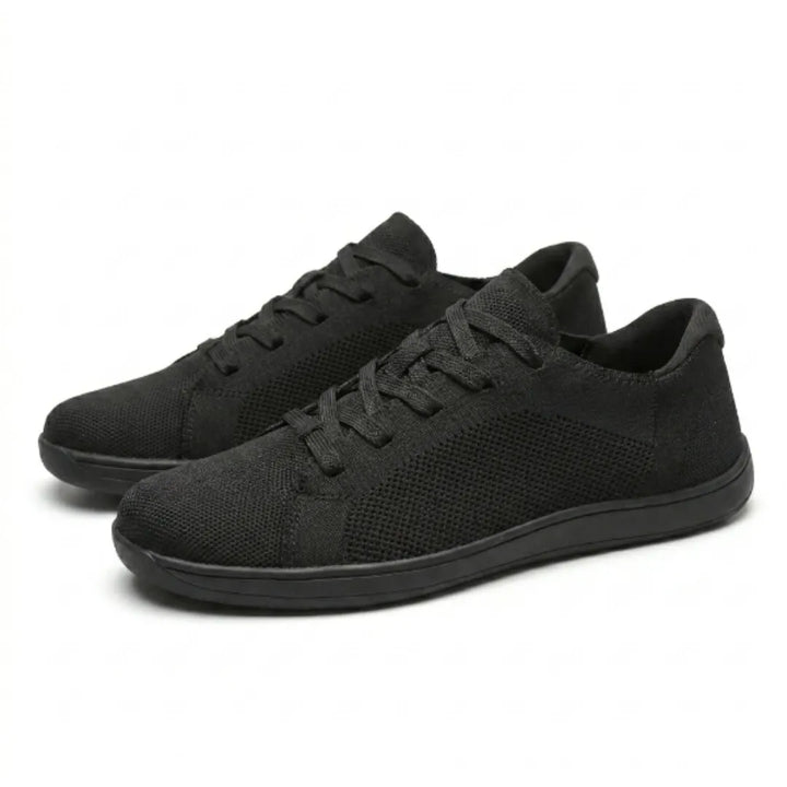 Paar schwarzer Mesh-Sneaker schräg von der Seite, nebeneinander stehend, mit Schnürung und flacher schwarzer Sohle. 16