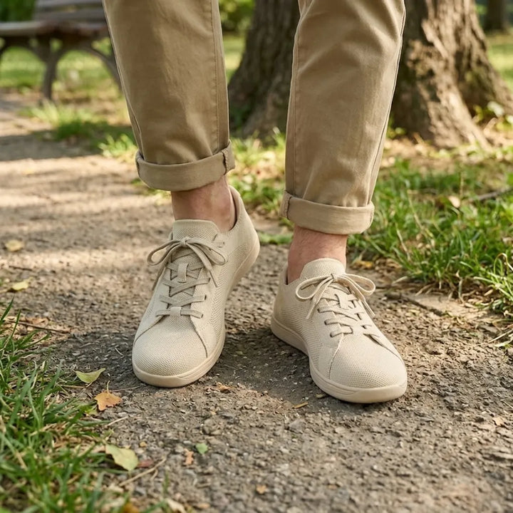 Beige Sneaker getragen auf einem Parkweg, dazu hochgekrempelte beige Hose, Gras und Baumstamm im Hintergrund. 2