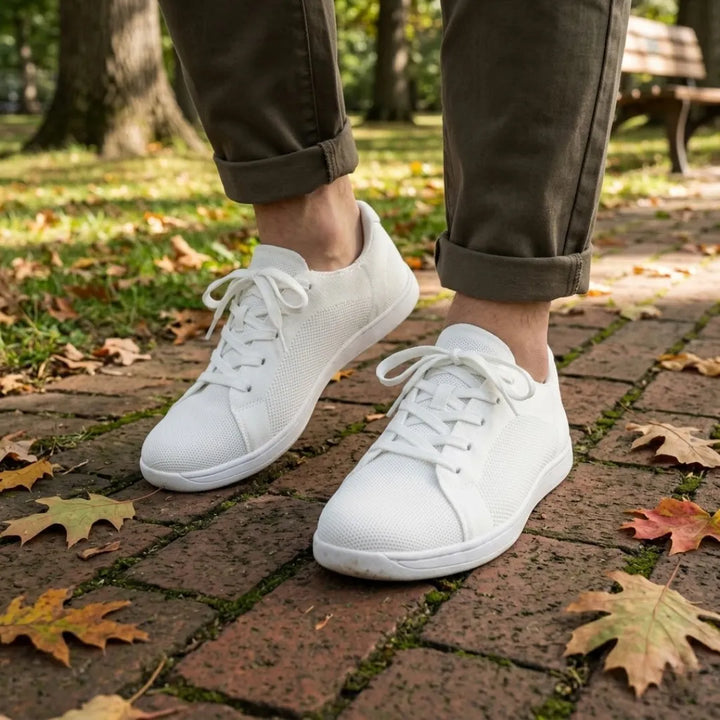 Person in olivgrüner Hose mit hochgekrempelten Hosenbeinen trägt weiße Mesh-Sneaker auf einem Backsteinweg mit Herbstlaub im Park. 38