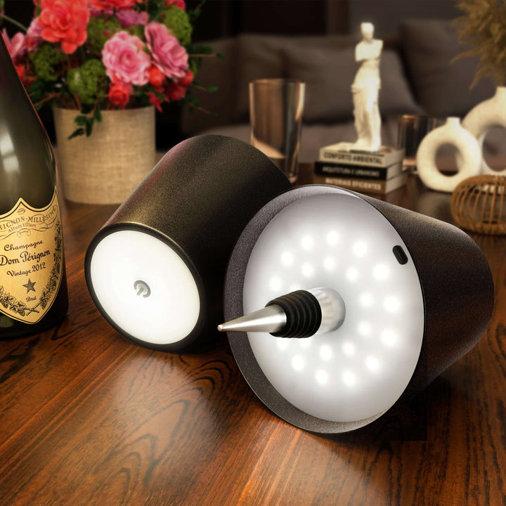 Moderne schwarze LED-Tischlampe auf Holztisch, umgeben von Dekoration und Champagnerflasche.