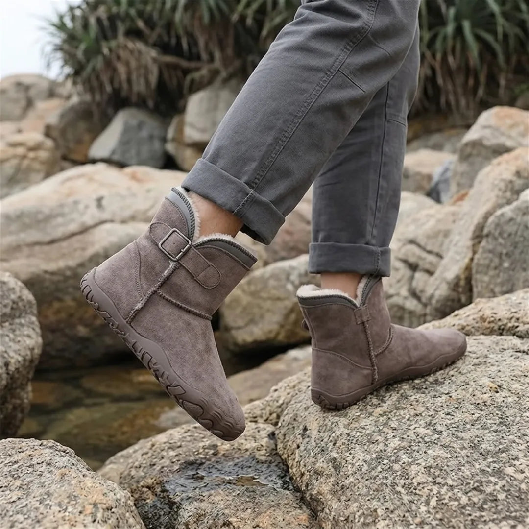 Taupefarbene Fellstiefel an den Füßen einer Person, die auf Felsen am Wasser läuft 38