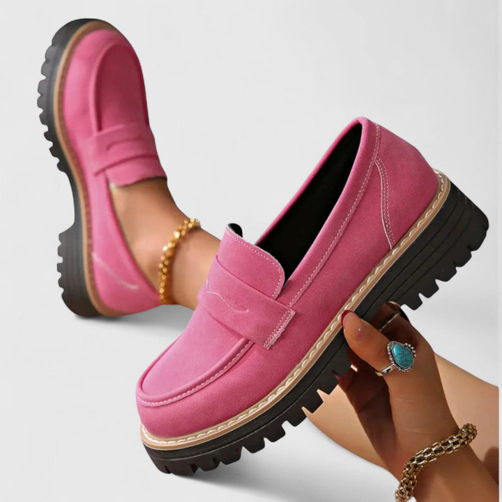 Pinkfarbene Loafer, ein Schuh in der Hand gehalten, der andere am Fuß, mit Goldarmband 3