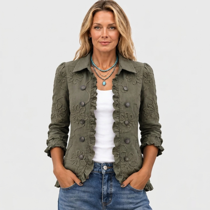 Frontansicht der olivgrünen Jacke am Model, mit Hemdkragen, Blumenstickerei und Rüschenbesatz, kombiniert mit weißem Top und Jeans. 2