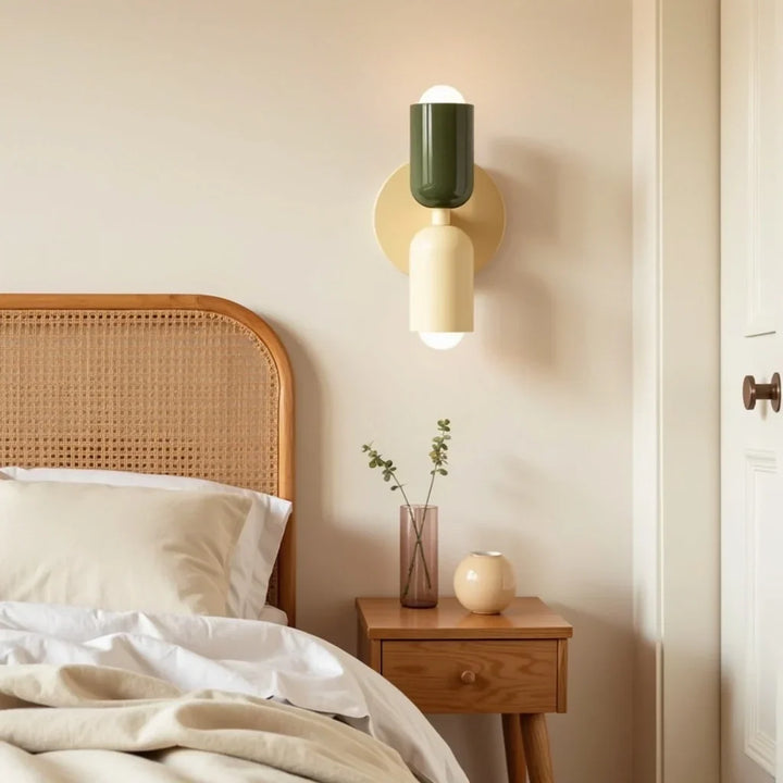 Wandlampe mit dunkelgrünem oberem und cremefarbenem unterem Schirm neben einem Bett mit Rattan-Kopfteil über einem Holz-Nachttisch mit Vase. 13
