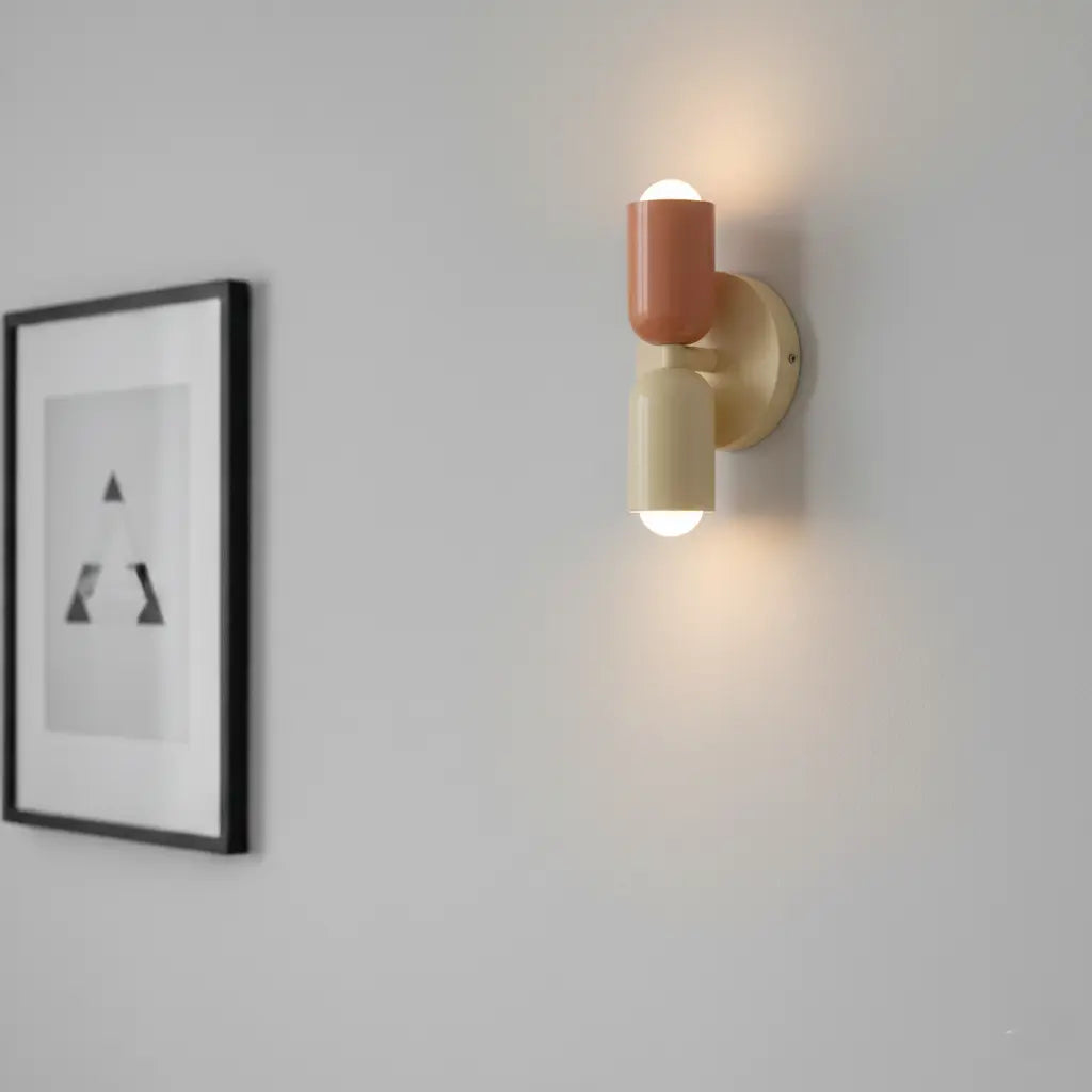 Eingeschaltete Wandlampe in Lachs und Creme an einer hellgrauen Wand, daneben ein schwarz gerahmtes Bild mit grafischem Motiv. 4