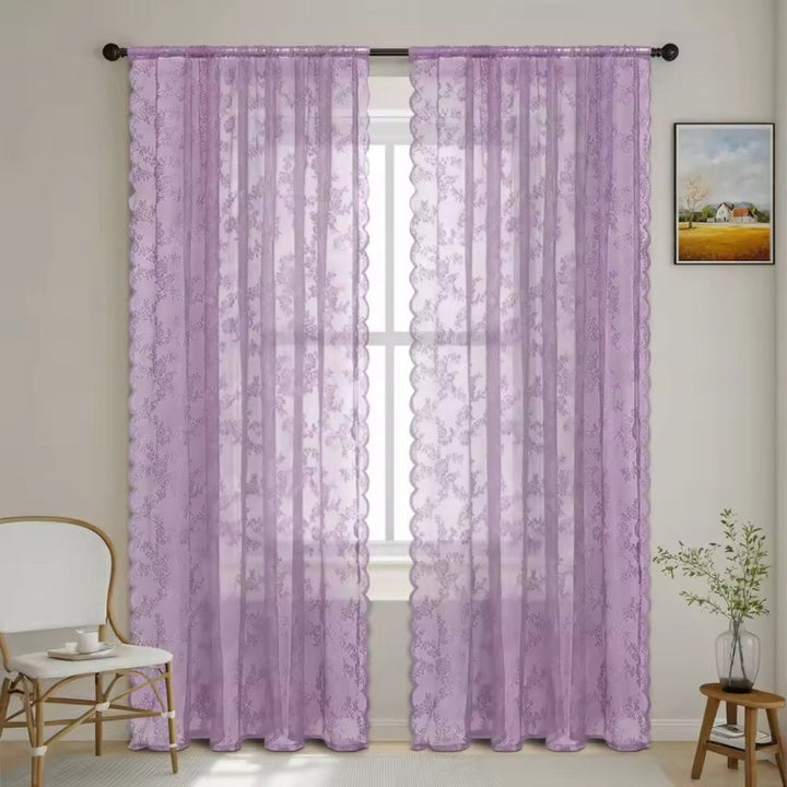 Zwei fliederfarbene Spitzenpaneele mit Blumenmuster und Wellenkante hängen an einer Stange vor einem Fenster im hellen Zimmer. 10