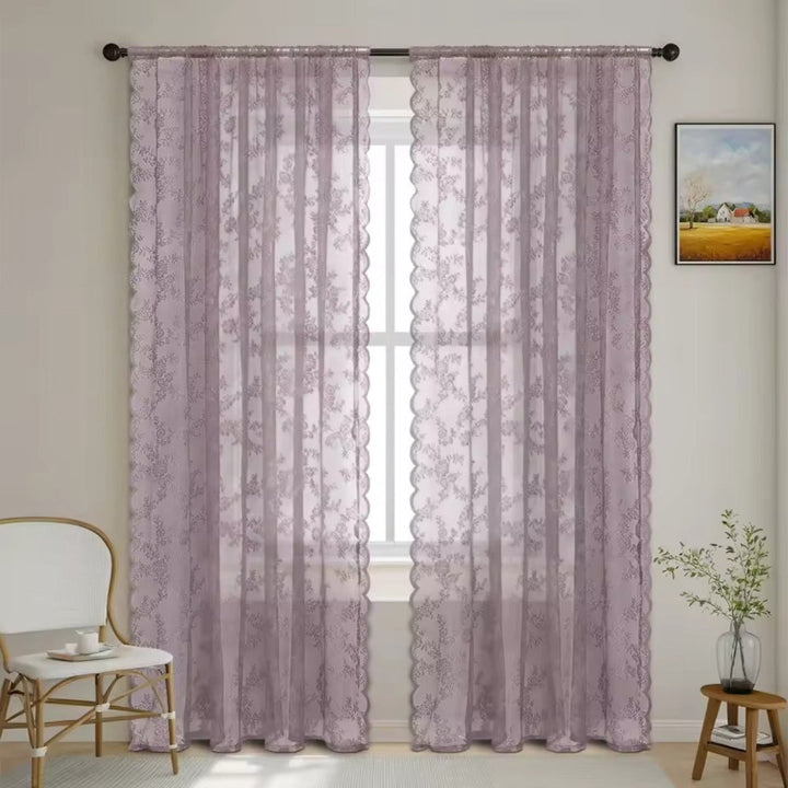 Zwei mauvefarbene Spitzenpaneele mit Blumenmuster hängen vor einem Fenster, daneben ein Rattanstuhl und ein Holzhocker mit Vase. 11