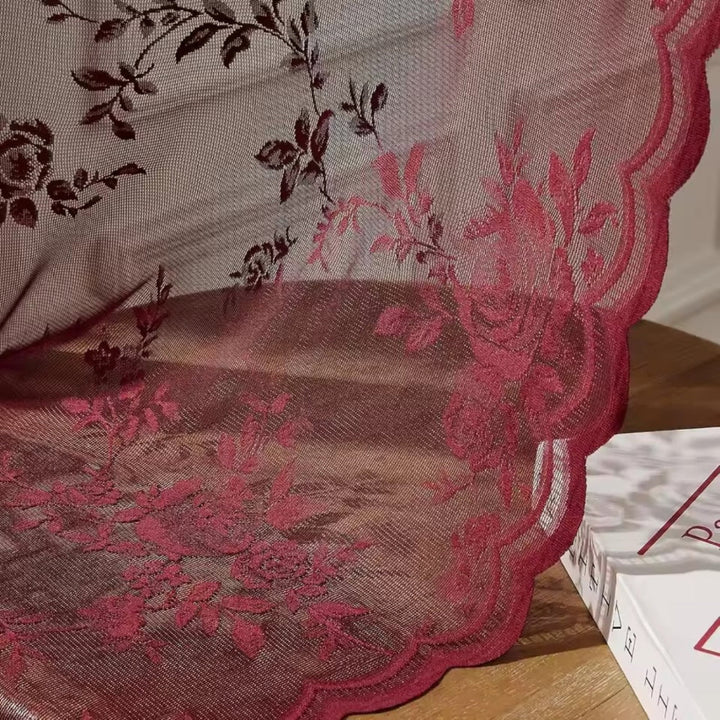 Nahaufnahme der weinroten Spitze mit Rosenranken und gewellter Kante, die auf einem Holztisch neben einem Buch aufliegt. 3