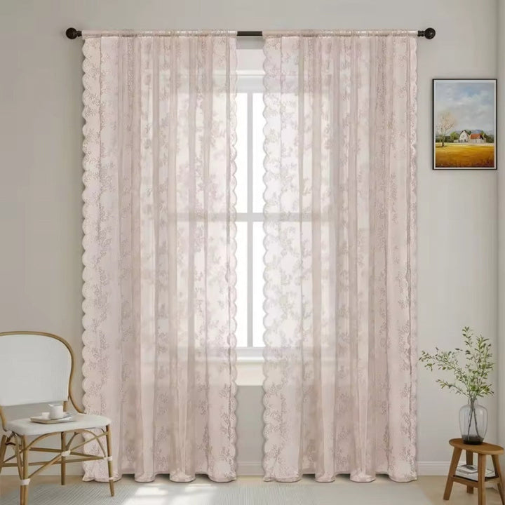 Zwei zartrosa Spitzenpaneele mit feinem Blumenmuster und Wellenkante hängen vor einem Fenster neben Stuhl und Pflanze. 9
