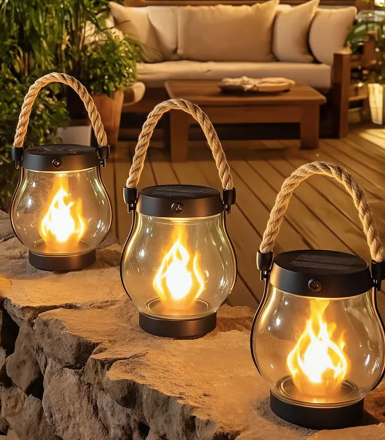 Drei leuchtende Glaslaternen mit Seilgriff und flackernder Flamme stehen abends auf einer Steinmauer vor einer Terrasse 1