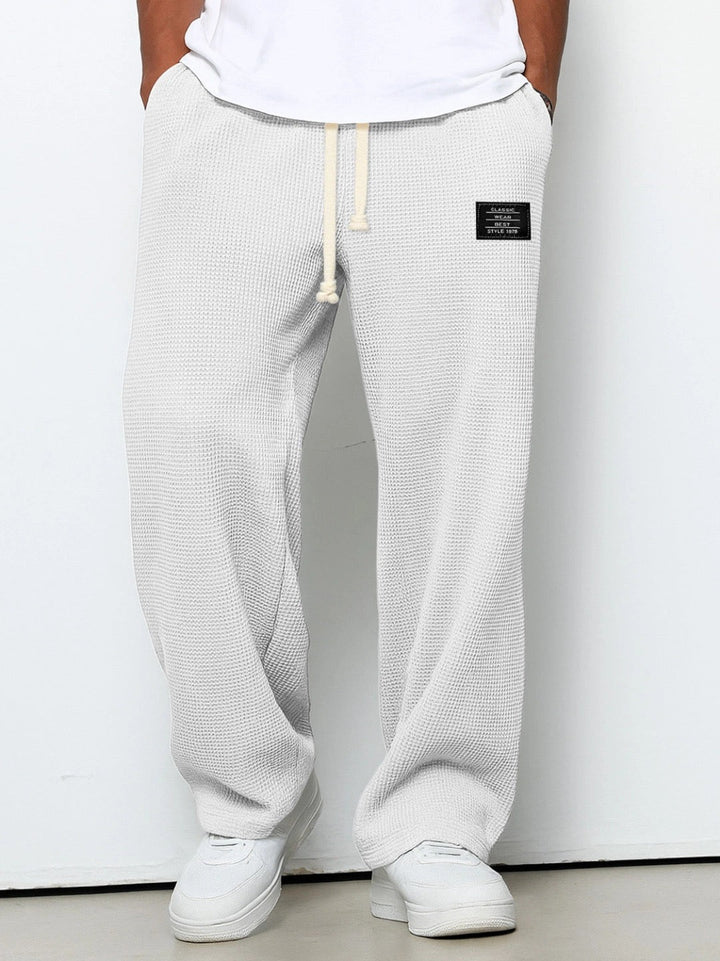 Dieselbe Hose in sehr hellem Grau oder Weiß an einem Model, mit cremefarbenem Kordelzug und weitem Bein. 2