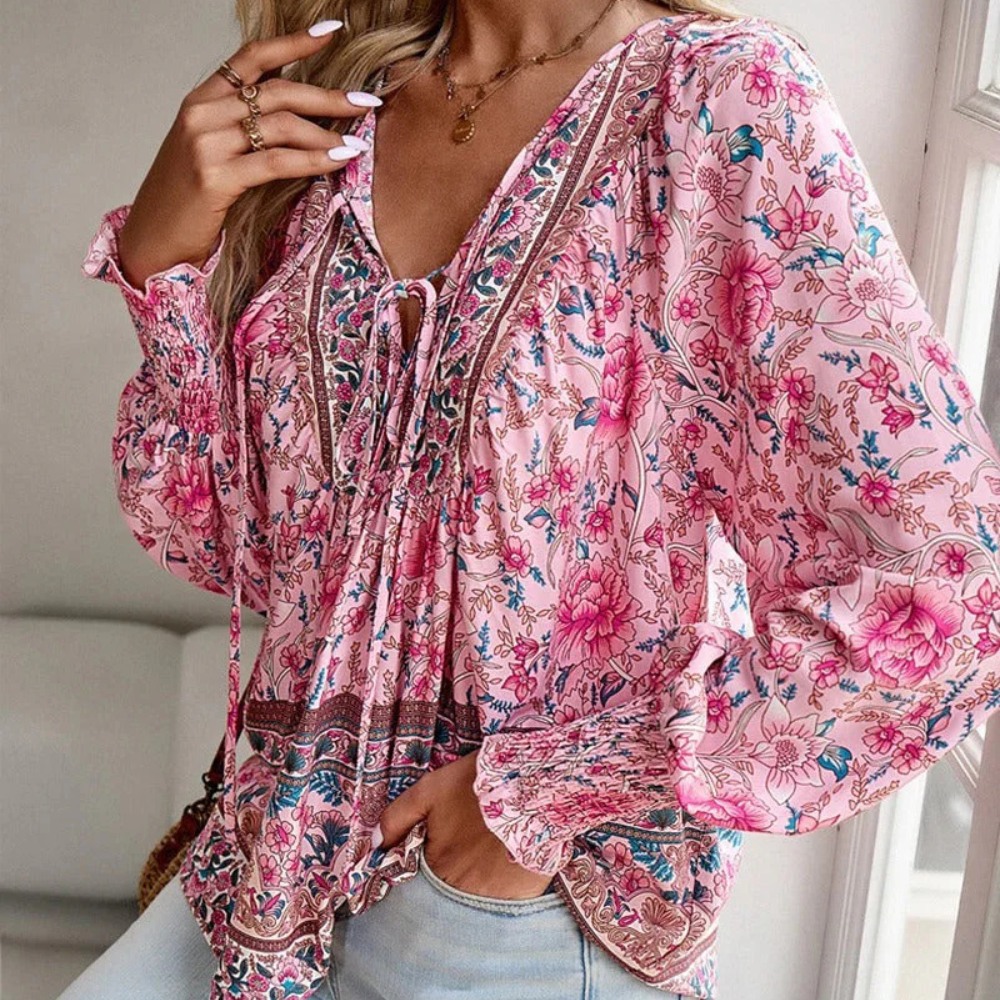 Frau trägt rosa geblümte Bluse, V-Ausschnitt, lange Ärmel, Boho-Stil, modisch, elegant.