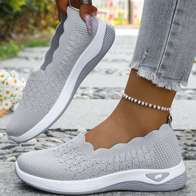 Graue Slip-ons aus Strick, ein Schuh getragen, der andere mit manikürter Hand angehoben 10