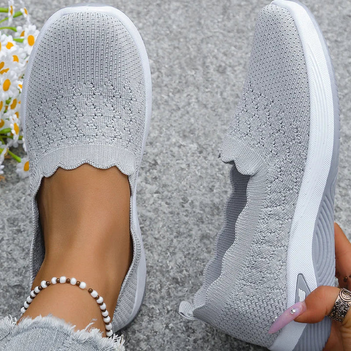 Draufsicht auf graue Strick-Slip-ons mit Lochmuster und Wellenrand auf grauem Untergrund 11