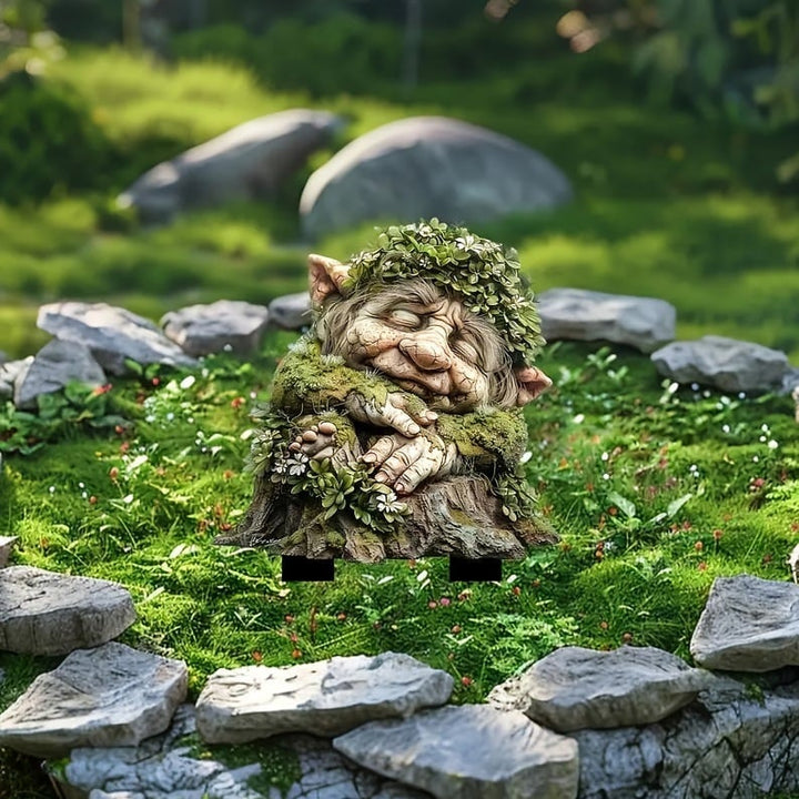 Schlafender Troll mit Blätterkranz auf Baumstumpf, mit schwarzen Steckfüßen auf einer Moosfläche mit Steinen aufgestellt. 18