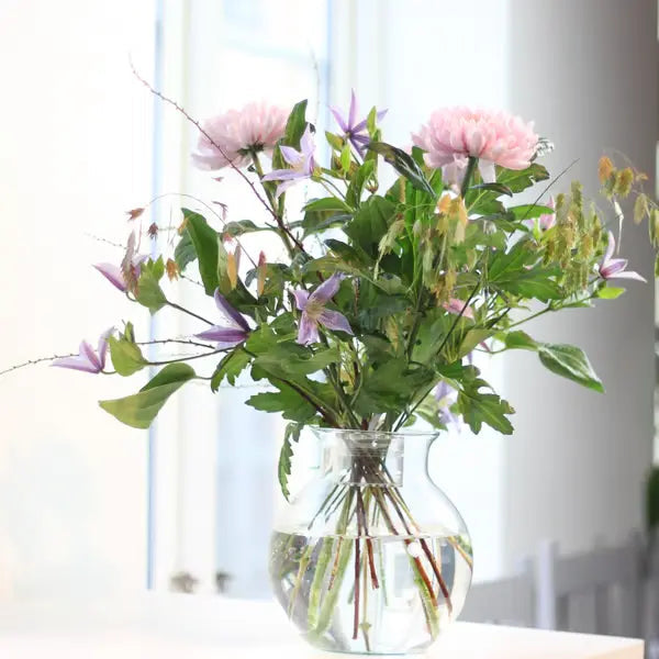 Lockerer Strauß mit rosa Dahlien und lila Clematis in einer runden Glasvase, im Wasser kreuzen sich die Stiele. 4