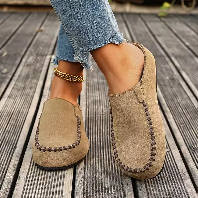 Beigefarbene Slipper mit brauner Ziernaht, getragen beim Gehen auf Holzdielen, ein Schuh seitlich, der andere von vorn. 5