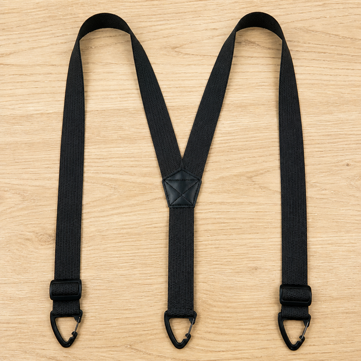 Schwarze Y-Hosenträger mit Verstellern direkt über den Klammern und kleinem Mittelstück, auf hellem Holz ausgebreitet. 13